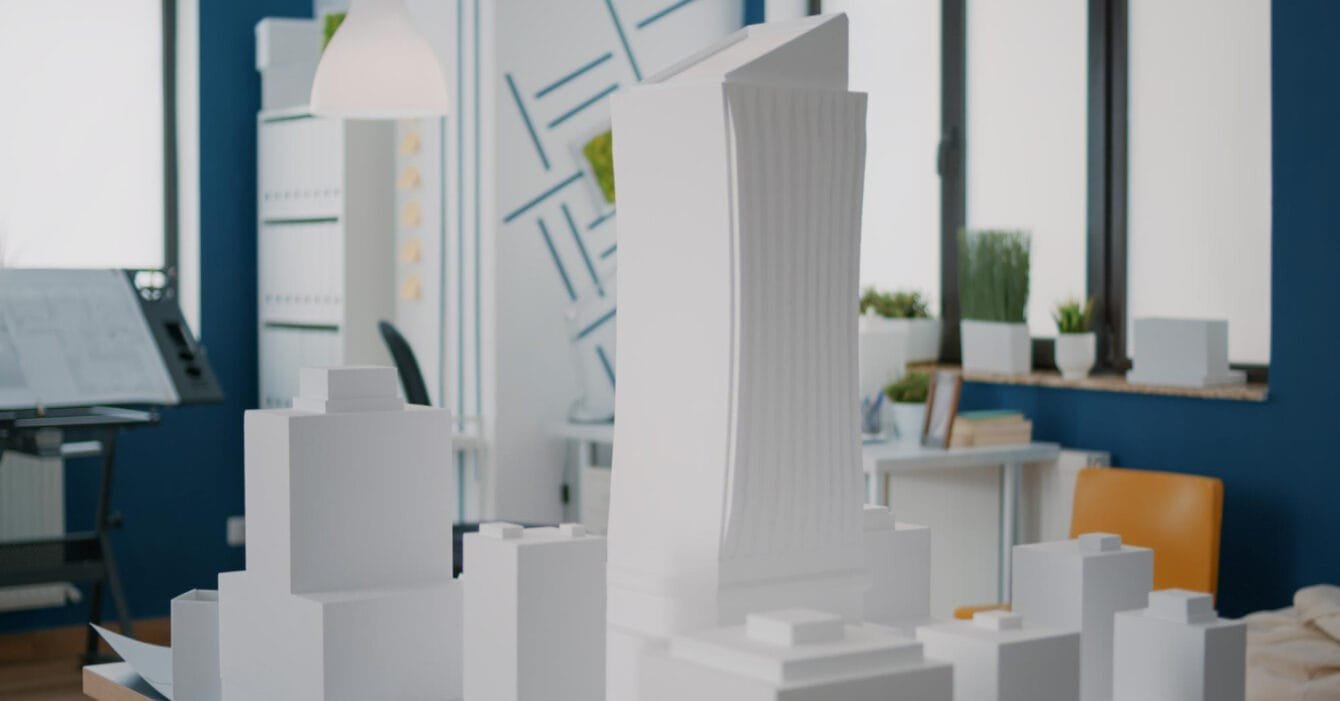 3D printed buildings Saudi Arabia: A model cityscape featuring a tall, modern building among smaller white structures, set in a stylish contemporary workspace.