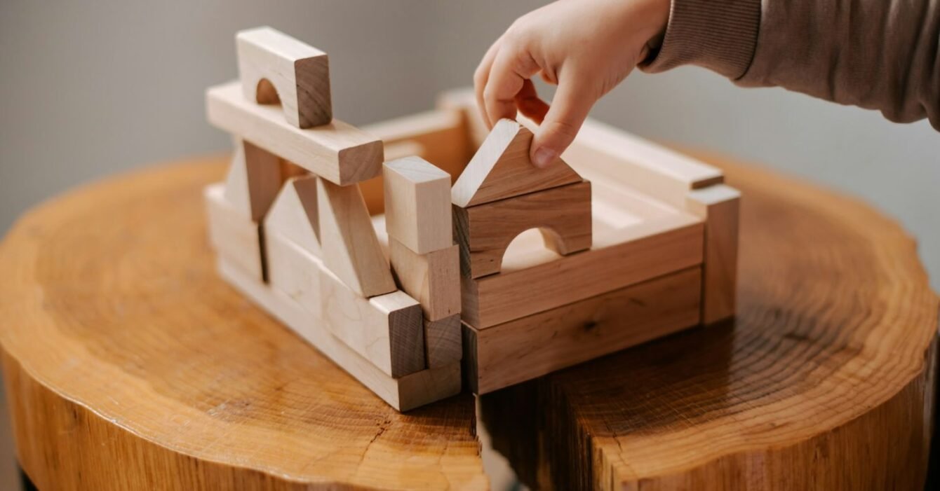 kateryna-hliznitsova-QqagtGFk4OM-unsplash Modular construction in Saudi Arabia: A child's hand places a wooden block on a structure made of building blocks atop a rustic wooden tabletop.