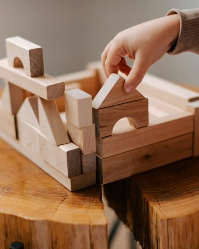 kateryna-hliznitsova-QqagtGFk4OM-unsplash Modular construction in Saudi Arabia: A child's hand places a wooden block on a structure made of building blocks atop a rustic wooden tabletop.